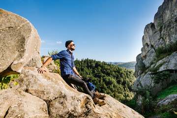 A traveler man with backpack and sunglasses sitting on the rocks at the mountais