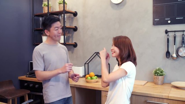 Beautiful happy asian couple are dancing in the kitchen at home. Young asian couple have romantic time while listening music at home.