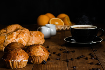 Breakfast set of hot coffee with croissant, banana cake and fresh orange fruits on wooden table with dark background