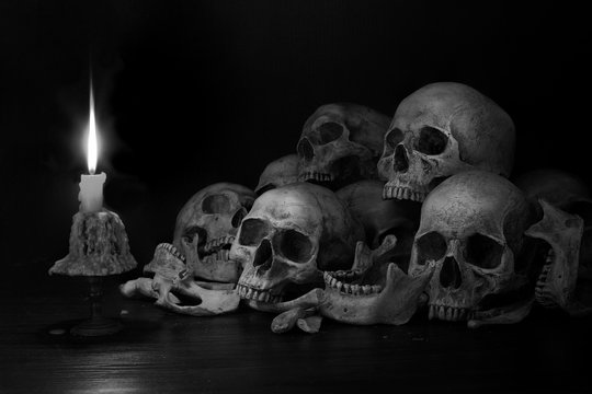Pile of skulls with bones and Candle which has flame to be bright in the dark light room
