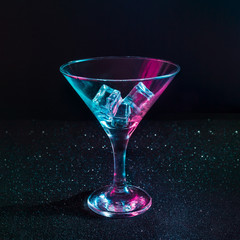 Martini glass filled with ice cubes in neon iridescent pink and blue colors. Minimal night party...