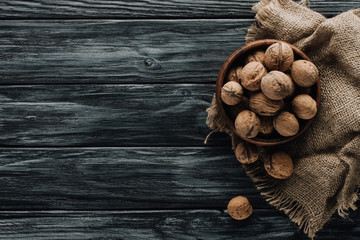 brown walnuts in wooden bowl on dark wooden surface