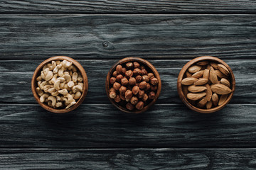 various nuts in three bowls on dark wooden table
