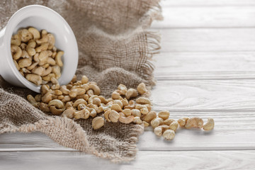 cashew in white ceramic bowl on sackcloth and white wooden tabletop