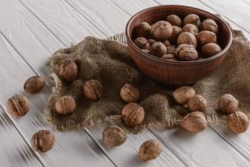 walnuts with wooden bowl and sackcloth on white wooden background
