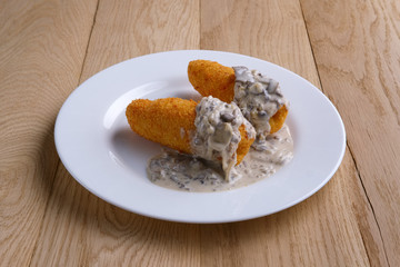Potato cutlet in breading stuffed with ham served with mushroom sauce