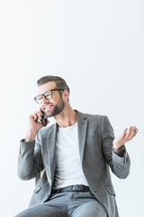 Fototapeta premium handsome businessman in gray suit gesturing and talking on smartphone, isolated on white