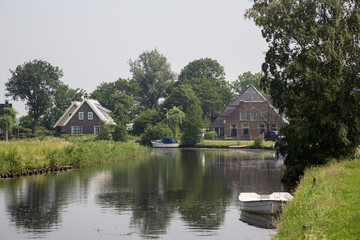 Fototapeta na wymiar Canal with buildings and small boat, Friesland, Netherlands