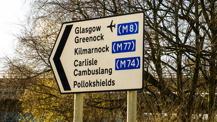 Road directional sign for Glasgow airport, Greenock, Kilmarnock, and Carlisle.