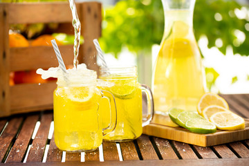 Filling fresh lemonade in mason jar glass on wooden table outside