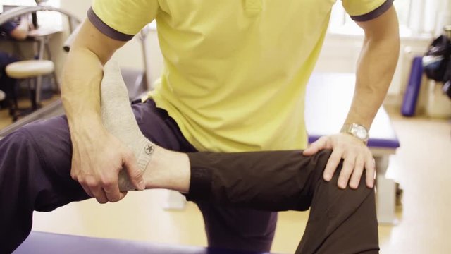 Close up hands of doctor physiotherapist helping disabled man, doing leg exercises at the rehabilitation center. Health reductive gymnastics.