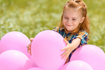portrait of smiling adorable child with pink balloons in summer field