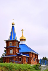 Fototapeta na wymiar Wooden church with domes. Wooden сhurch with blue roof and golden domes. The structure is built of logs. Blue metal fence.