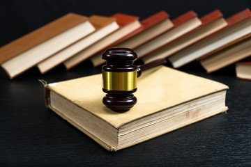 Judge gavel beside pile of books on black wooden background