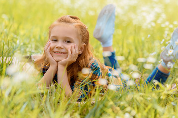 portrait of little smiling child resting on green grass in meadow
