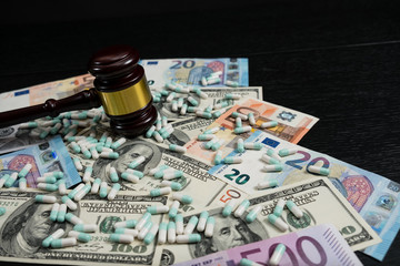Wood judge's gavel and scattered colorful drugs on the dollar and euro cash background, drugs falsification, concept for medical negligence, bail. Overhead view.