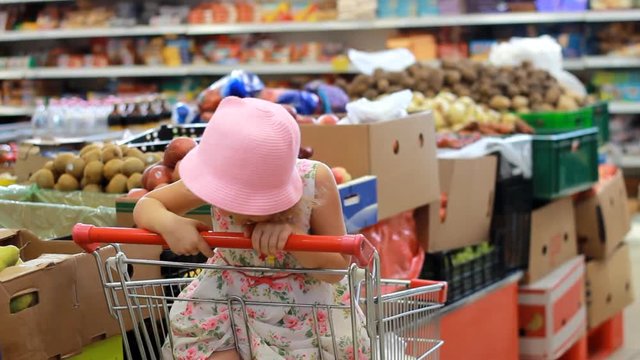 Child girl in the store chooses fruit. Grocery supermarket and shopping trolley