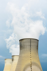 Three natural draft cooling towers of a nuclear power plant releasing clouds of water vapor against a dark stormy sky.