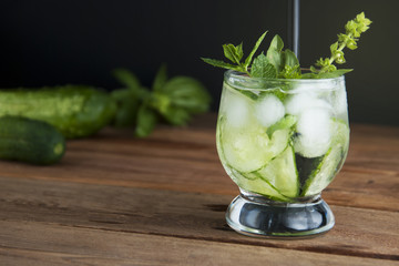 Cold fresh lemonade with cucumber, ice and mint leaves over wooden table and black background. Fresh summer drink in glass. Copy space.