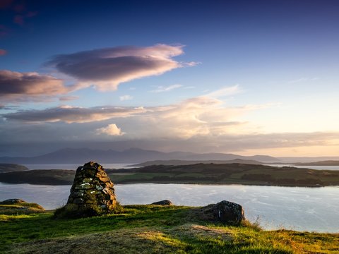 Just before sunset looking over the Cumbrae Isles towards Arran, on the West coast of Scotland. A stone cairn is prominent in the foreground