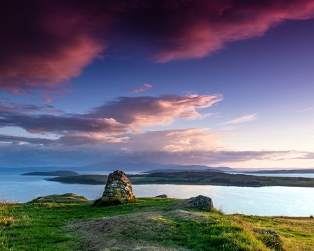 Just after sunset looking over the Cumbrae Isles towards Arran, on the West coast of Scotland. A stone cairn is prominent in the foreground