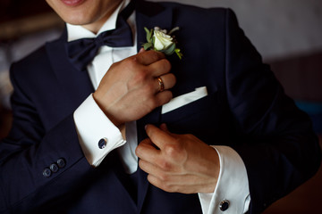 stylish man in black suit and white shirt corrects the boutonier. the groom hands with a boutonier...