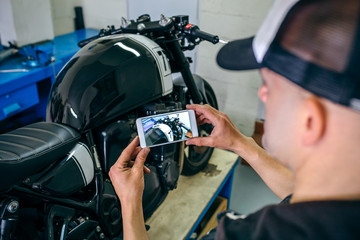 Mechanic taking picture of customized motorcycle just finished in the workshop