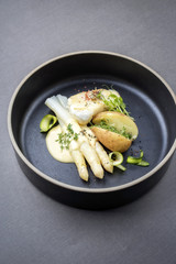 Modern German fried cod fish filet with white asparagus in hollandaise sauce und roast potatoes as top view on a plate