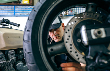 Mechanic fixing custom motorcycle wheel in his workshop. Selective focus on mechanic in background
