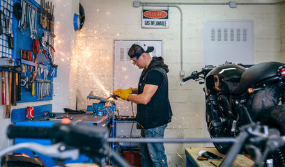 Young motorcycle mechanic using a grinder in the workshop - Powered by Adobe