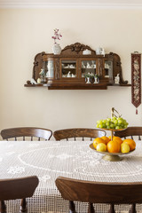 Wooden chairs at table with fruits in white classic dining room interior with shelves. Real photo