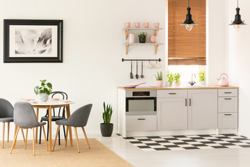 Real photo of open space kitchen interior with dining table with chairs, window with wooden blinds...