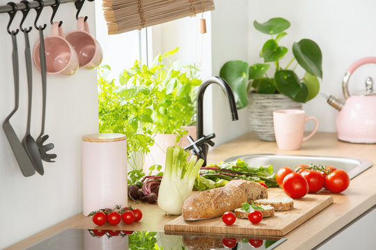 Fresh vegetables and bread placed on countertop in real photo of kitchen interior with pastel pink kettle and mugs