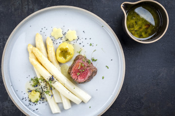 Modern German barbecue dry aged sliced fillet steak with white asparagus and roast potatoes in butter sauce as top view on a plate