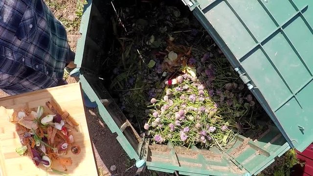 Farmer throwing out kitchen waste to the garden compost heap for recycling and fertilizer. Slow motion.