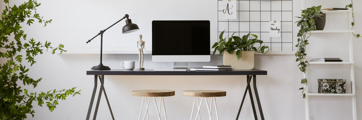 Black desk with lamp, tea cup, notebooks and mockup screen monitor in real photo of bright living...