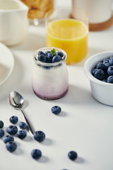 close up view of healthy yogurt with fresh blueberries and glass of juice for breakfast on white tabletop