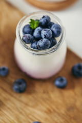 close up view of yogurt with fresh blueberries for breakfast on wooden cutting board