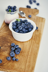 close up view of fresh blueberries and yogurt for breakfast on wooden cutting board