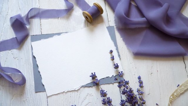 White blank card, envelope and ribbon on a background of pink and blue fabric with lavender flowers on a white background. Mockup with envelope and blank card. Flat lay. Top view
