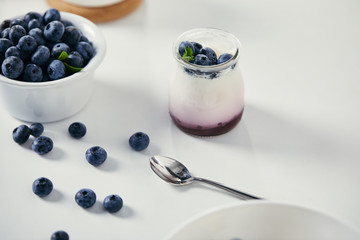close up view of fresh blueberries and yogurt for breakfast on white tabletop with spoon