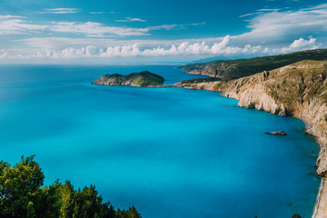 Fototapeta na wymiar View of Kefalonia west coastline. Assos village town and Frourio peninsular. Beautiful milky blue bay with brown rocky limestone costline and moving white clouds on horizon. Greece