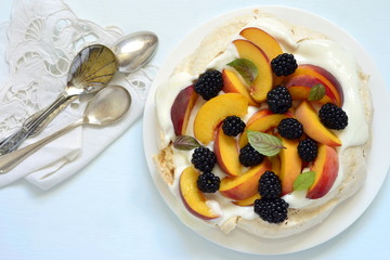 Pavlova with fresh fruit and berries - blackberries and peaches on a blue background, top view, copy space
