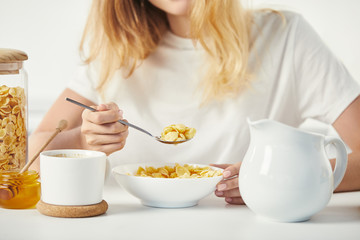 partial view of woman at table with corn flakes, honey and cup of coffee for breakfast