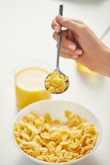 partial view of woman at table with corn flakes and glass of juice for breakfast