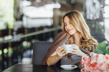 Young pretty girl blonde in casual clothes resting and drinking coffee on a summer terrace cafe. She was presented with a bunch of roses.