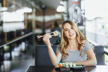 A young beautiful blond girl eating sushi on the summer terrace of a Japanese restaurant