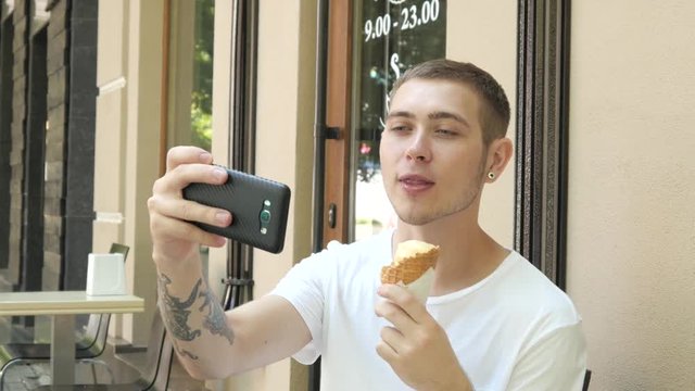Young Handsome Man eating an Ice Cream Scone on the Street, makes Selfie Photo