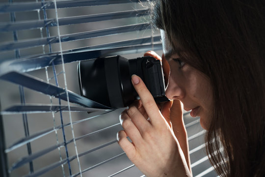 Young woman Paparazzi take a photo suspiciously from around a blinds  while using a camera. GDPR Concept