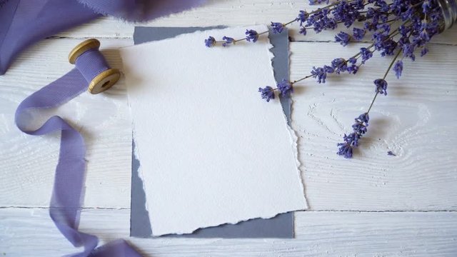 White blank card, envelope and ribbon on a background of pink and blue fabric with lavender flowers on a white background. Mockup with envelope and blank card. Flat lay. Top view